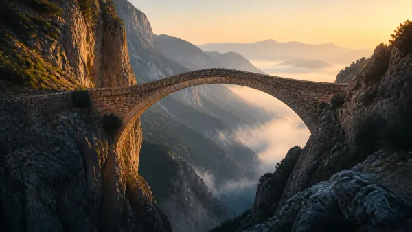 Ancient stone arch footbridge spanning a deep misty mountain gorge, connecting two rugged cliffs under clear golden morning light