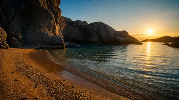 Sheltered tranquil ocean cove with smooth golden sand and calm water protected by towering dark coastal cliffs at sunrise