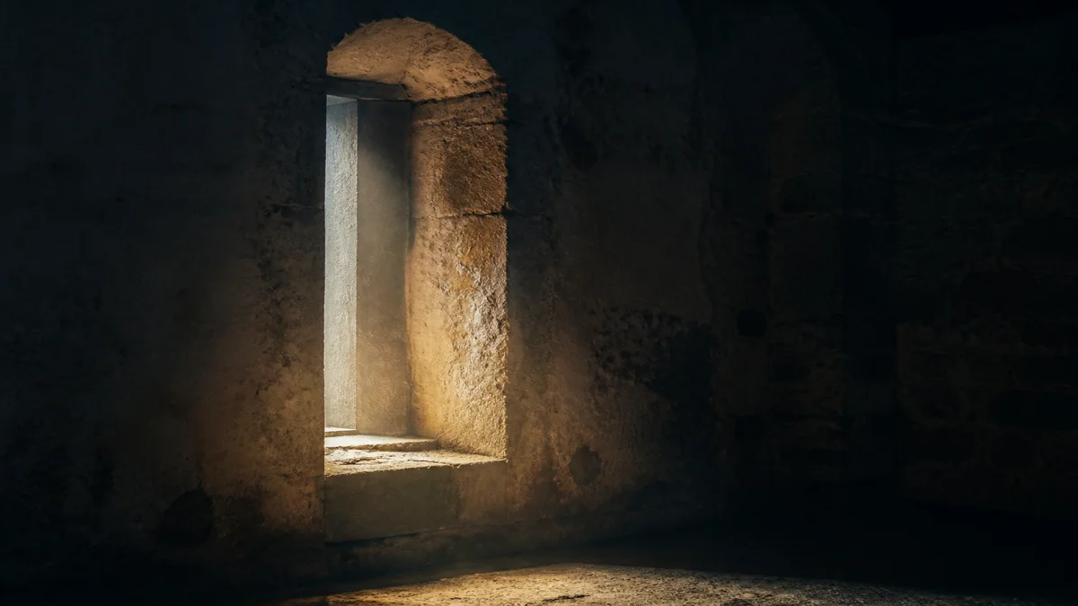 A narrow window set deep in a thick stone wall with first daylight reaching the sill of an otherwise dark room